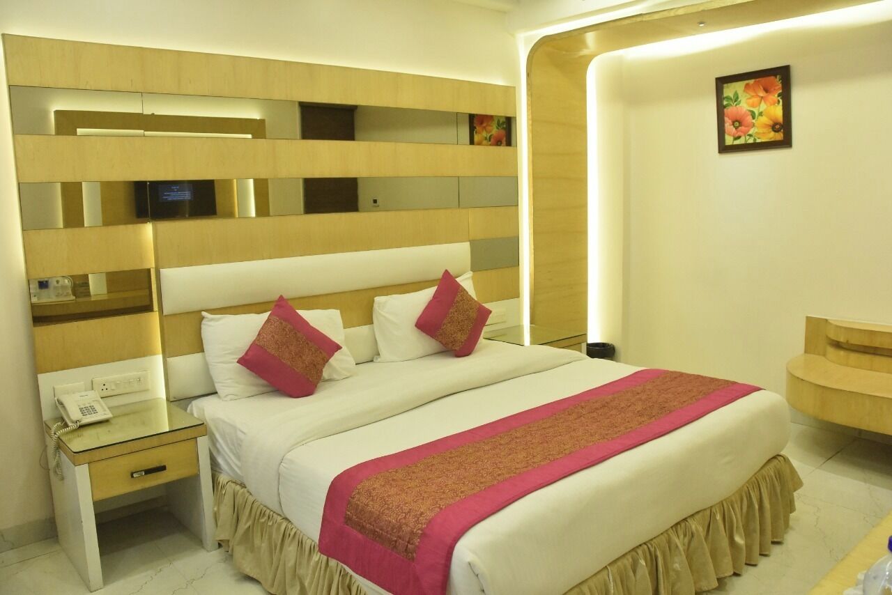 A hotel room with a large bed, a bedside table with a phone, a mirror above the bed, and a small desk with a lamp.