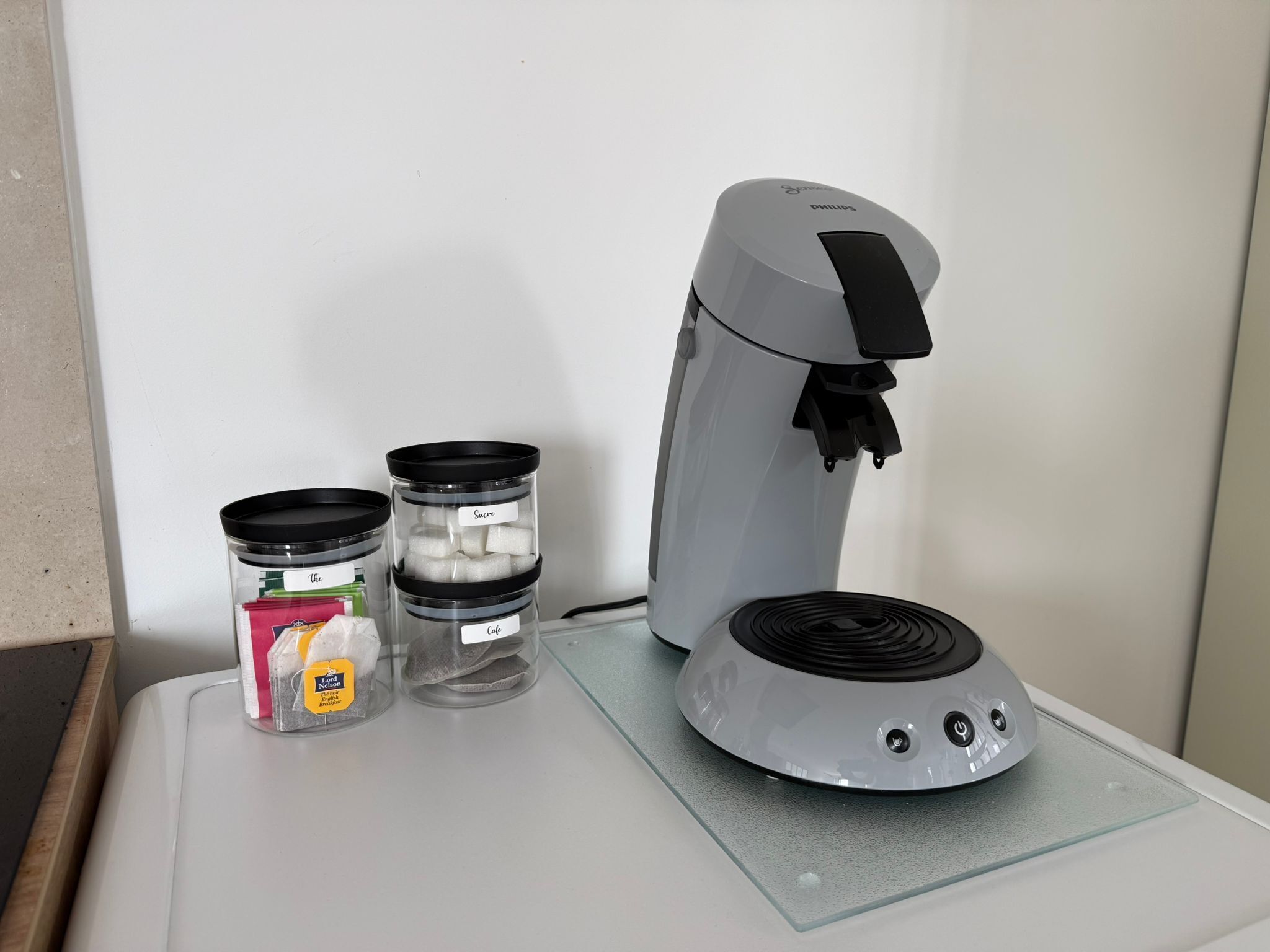 A coffee maker with a glass carafe and two containers labeled "Sugar" and "Coke" on a countertop.
