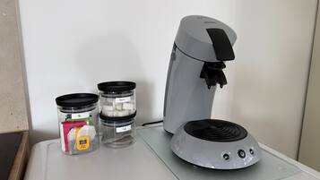 A coffee maker with a glass carafe and two containers labeled "Sugar" and "Coke" on a countertop.