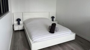 A single-bed room with a white headboard, two bedside tables with lamps, and a rolled towel on the bed. - Spacious and Bright New T3 (Évreux)