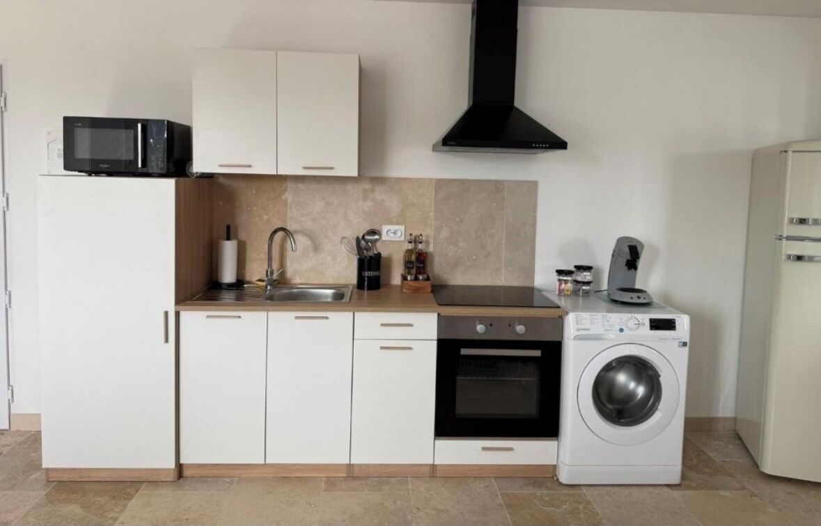 Een kleine keuken met witte kastjes, een magnetron, een spoelbak, een kookplaat en een wasmachine.