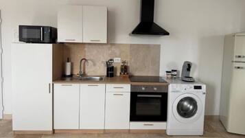 Een kleine keuken met witte kastjes, een magnetron, een spoelbak, een kookplaat en een wasmachine.