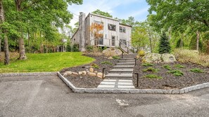 A modern house with a stone staircase leading to the entrance, surrounded by a well-maintained garden and trees. - Chic East Hampton Retreat with Private Pool, Private Yard, and Resort-Style... (East Hampton)