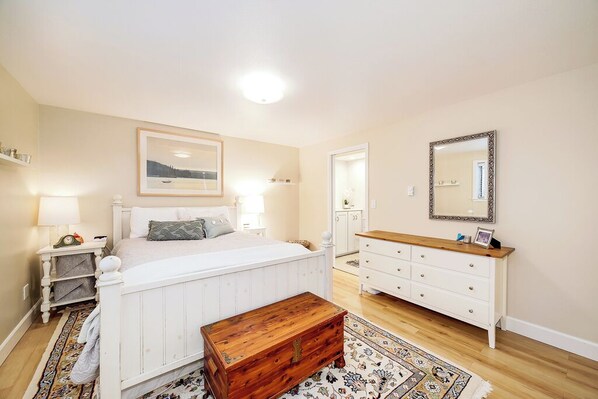 A bedroom with a bed, bedside tables, a dresser, a mirror, and a painting on the wall.