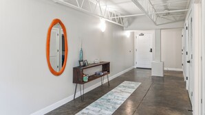 A hallway with a wooden console table, a large mirror with an orange frame, and a white door at the end. - Relax & Recharge 1br Downtown Loft w Private Patio (Des Moines)