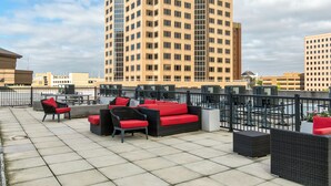 An outdoor seating area with wicker furniture and red cushions, overlooking a cityscape with tall buildings. - Relax & Recharge 1br Downtown Loft w Private Patio (Des Moines)