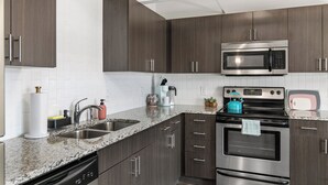A modern kitchen with dark wood cabinets, stainless steel appliances, and a granite countertop. - Relax & Recharge 1br Downtown Loft w Private Patio (Des Moines)