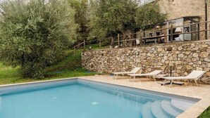 A swimming pool with lounge chairs, surrounded by a stone wall and greenery. - Charming Tuscany Villa w/ Private Infinity Pool (Castel del Piano)