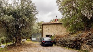 A stone building with a car parked in front, surrounded by trees and a gravel path. - Charming Tuscany Villa w/ Private Infinity Pool (Castel del Piano)