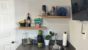 Een kleine keuken met een vaatwasser, een spoelbak en een aanrecht met diverse items, zoals een koffiezetapparaat, een plant en keukengerei.