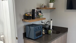 Een kleine keuken met een ingebouwde oven, een koffiezetapparaat en een waterkoker op het aanrecht.