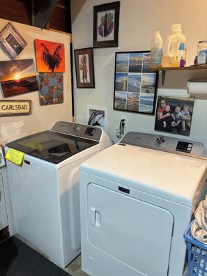 A laundry area with two washing machines, a wall-mounted shelf with personal items, and a framed collage of photos. - Lovely 1-bedroom studio in peaceful Santa Rosa perfect for your stay (Santa Rosa)