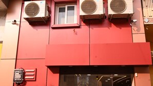 A hotel named 'TRINETRA HOME STAY' with a red facade, large air conditioning units, and a glass entrance. - Trinetra Homestay (Varanasi)
