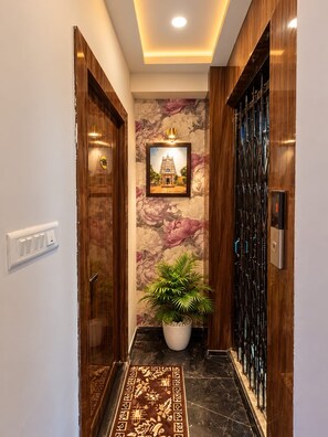 A hallway with a framed picture on the wall, a potted plant, and a patterned rug. - Trinetra Homestay (Varanasi)