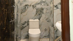 A bathroom with marble walls, a toilet, a sink, and a shower. - Trinetra Homestay (Varanasi)