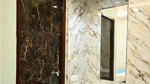 A bathroom with a marble vanity, a dark marble door, and a mirror. - Trinetra Homestay (Varanasi)