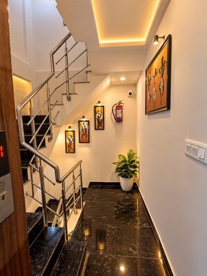 A modern interior with a staircase, framed artwork, a fire extinguisher, and a potted plant. - Trinetra Homestay (Varanasi)