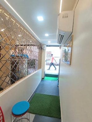 A narrow hallway with a metal partition, a green mat, and a red chair. - Trinetra Homestay (Varanasi)