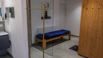 Une chambre avec un lit en bois, une cloison en verre, une petite étagère contenant des articles de toilette et une armoire en bois.
