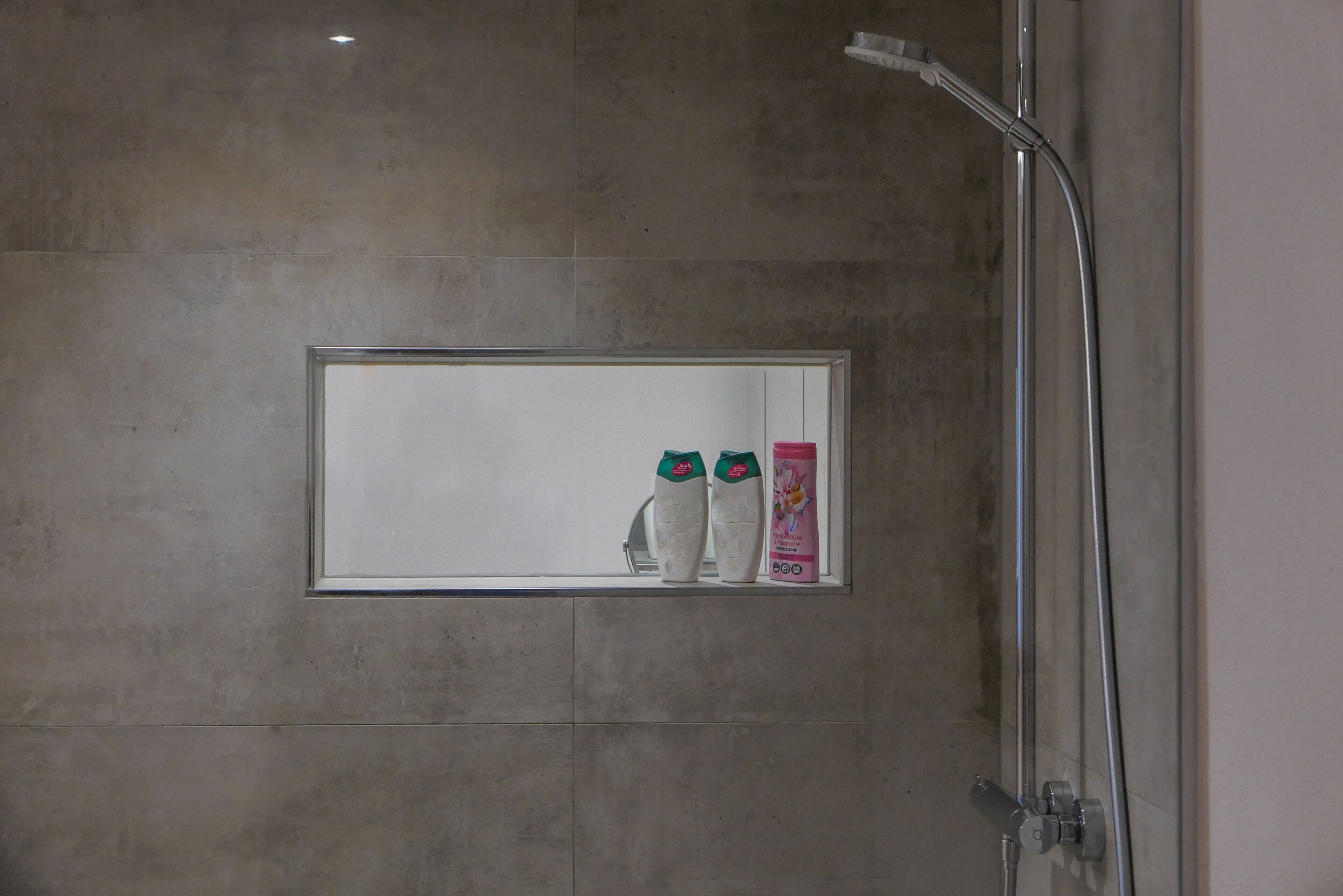 Um banheiro com chuveiro, espelho e duas garrafas de shampoo.