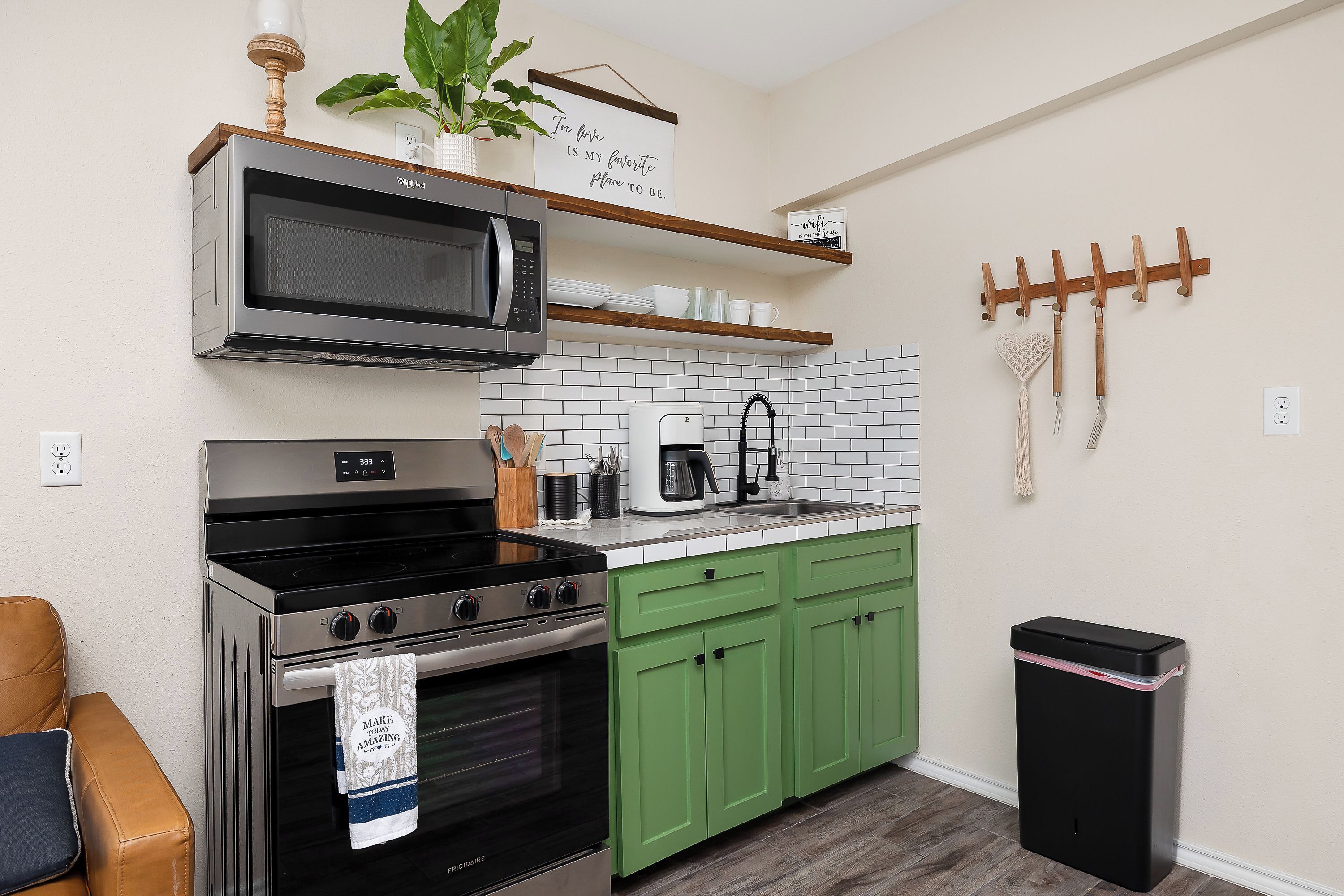 Une cuisine équipée d’un four à micro-ondes, d’une cuisinière et de meubles de rangement verts. On y trouve également une machine à café et une poubelle.