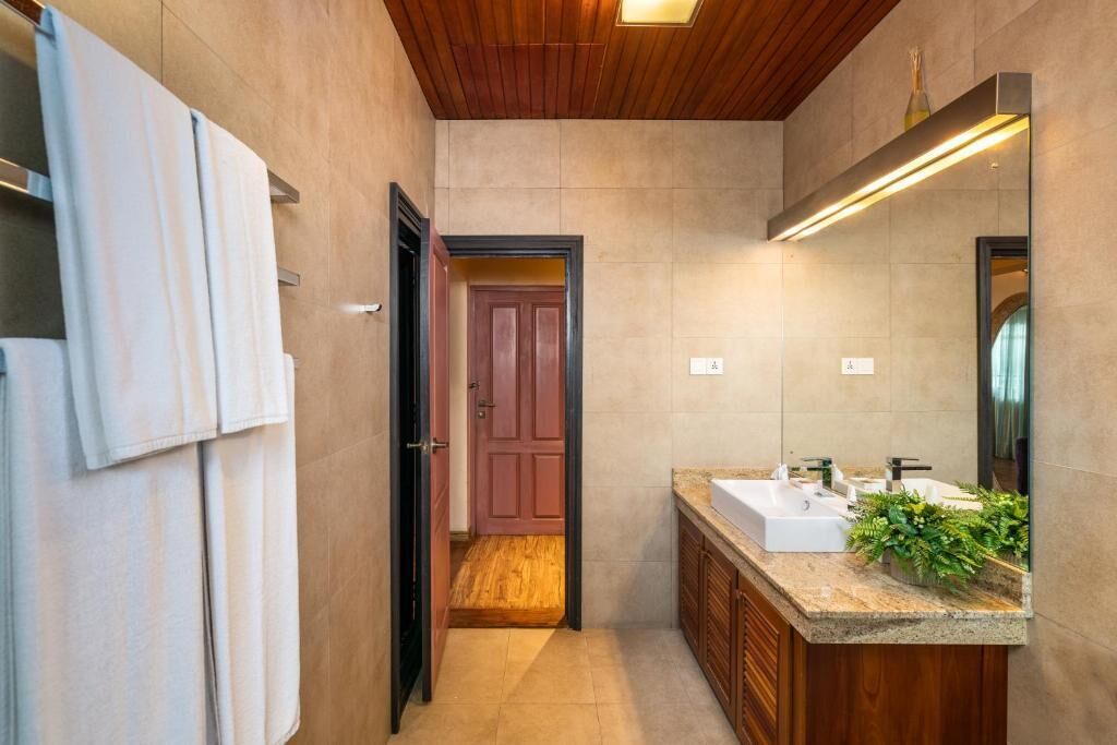 A modern bathroom with a wooden ceiling, a large mirror, a sink with a granite countertop, and a door leading to another room.