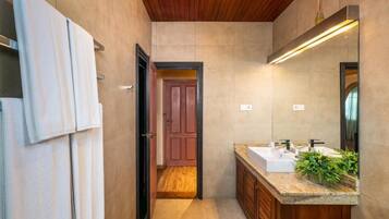 A modern bathroom with a wooden ceiling, a large mirror, a sink with a granite countertop, and a door leading to another room.