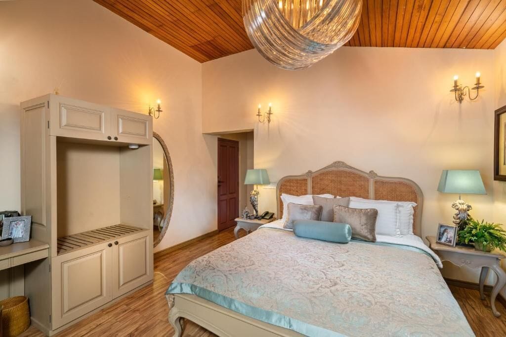 A bedroom with a large bed, a wardrobe, a mirror, and wall sconces.