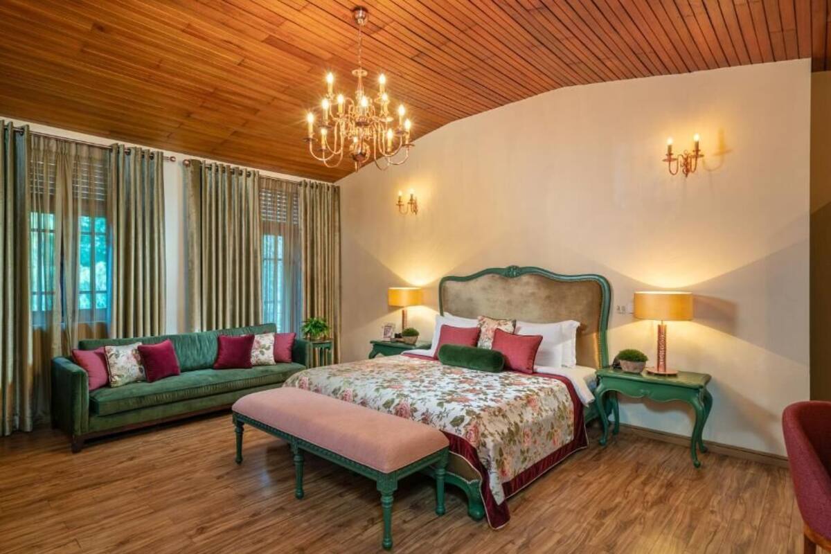Un dormitorio con una cama grande, un sofá verde, un banco y dos mesitas de noche con lámparas.