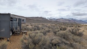 A stationary RV in a desert landscape with sparse vegetation and distant snow-capped mountains. - Dark Sky · Stargazer Horse Trailer · Edge of the Alvord Desert (Princeton)