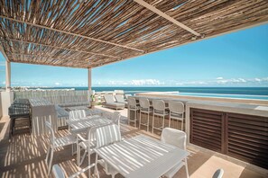 A covered outdoor seating area with tables and chairs, overlooking a beach and ocean. - Greta Luxury Design: Private Pool, Beachfront Bliss in Puerto Morelos! (Puerto Morelos)