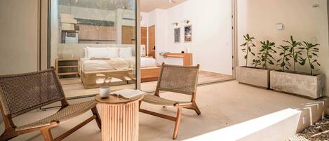 Een moderne kamer met een glazen deur naar een balkon, een houten stoel, een klein rond tafeltje en een bed met een houten hoofdeinde.