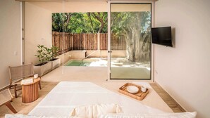 A bedroom with a large bed, a small table with a cup, a chair, and a TV on the wall. - Lujo Frente al Mar con Piscina Privada y Playa (Puerto Morelos)