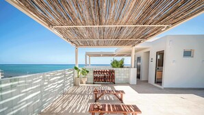Un'area esterna riparata con vista sul mare, con due tavoli di legno e un angolo relax.