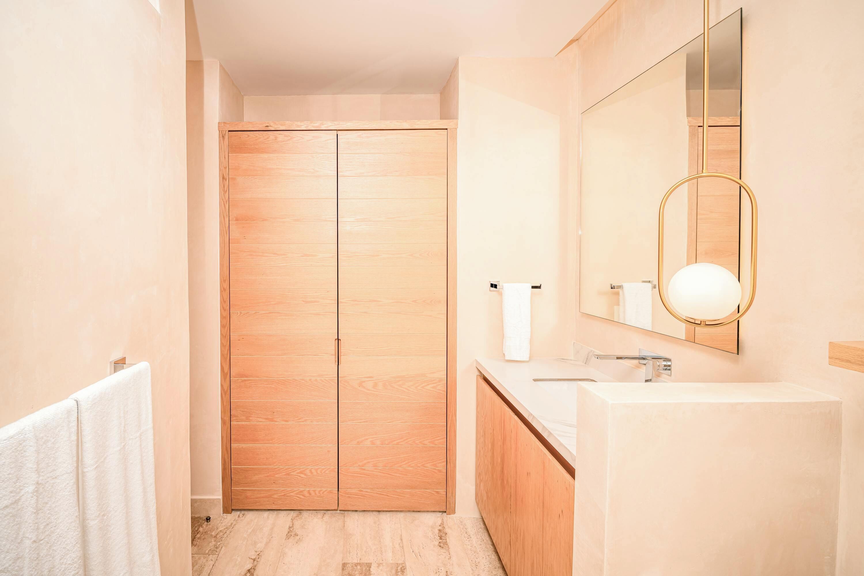 Een badkamer met een houten kledingkast, een wastafel en een spiegel met ronde verlichting.