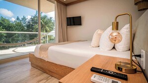 A modern hotel room with a large bed, a bedside table with a lamp, a TV mounted on the wall, and a view of the outdoors. - Luxury Oceanview with unique disign (Puerto Morelos)