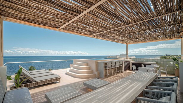 A rooftop terrace with a view of the sea, a bar area, and outdoor seating. - Modern Seafront Unit | Infinity Pool, Gym (Puerto Morelos)