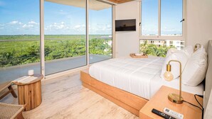 A modern bedroom with a large bed, a TV mounted on the wall, and a view of greenery outside. - Modern & Peaceful Getaway | Eco-Luxury in Greta (Puerto Morelos)
