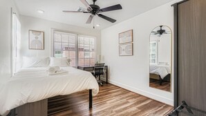 A bedroom with a bed, desk, chair, ceiling fan, and large windows. - Houston Hideaway Steps from Rice Village Fun (Houston)