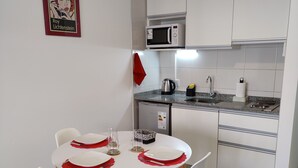 Ett modernt kök med vita skåp, en mikrovågsugn och en diskho. Det finns ett matbord med vita stolar och röda bordsunderlägg.