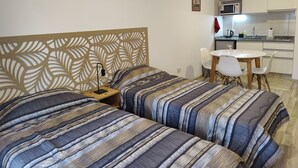 Ett hotellrum med två sängar, en sänggavel i trä, ett litet bord med stolar och ett litet kök i bakgrunden.