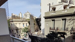 Un balcon donnant sur une rue animée, un sol carrelé et un climatiseur blanc.