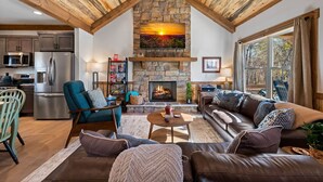 Ein Wohnzimmer mit Kamin aus Stein, Ledersofa, Holzbalkendecke und einer Küchenzeile mit modernen Geräten.