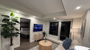 Una sala de estar moderna con un televisor de pantalla plana, una planta grande en maceta, una mesa de centro redonda de madera y un sofá con una manta.