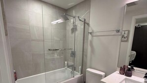 Un baño moderno con ducha de vidrio, inodoro blanco y tocador con espejo.