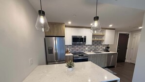 Una cocina moderna con una isla central, electrodomésticos de acero inoxidable e iluminación colgante.