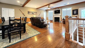 Un salón espacioso con zona de comedor, piso de madera, chimenea y escalera.