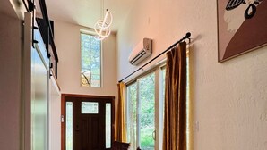 A spacious hallway with a wooden floor, a seating area with two chairs, and a large window with curtains. - Casita Lotus cozy little loft on an Orchard (El Paso)