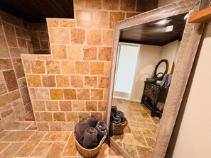 Un baño con paredes de piedra, un espejo, un banco de madera y dos cestas de toallas.