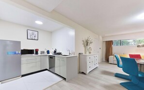 Eine moderne Küche mit weißen Schränken, einem Kühlschrank und einem Essbereich mit blauem Stuhl und einer Couch.